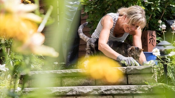 Eine Frau reinigt 2018 in einem Garten die Fugen zwischen den Steinplatten auf der Terasse.