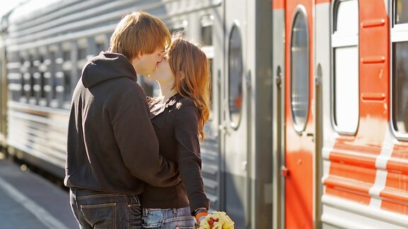 Ein junger Mann küsst eine junge Frau auf einem Bahnsteig