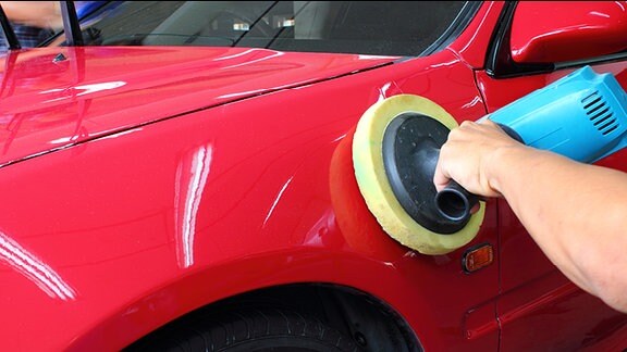 Ein rotes Auto wird mit einer Poliermaschine aufpoliert.