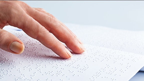 Finger fahren über eine Seite mit Brailleschrift
