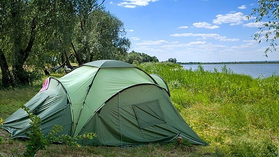 Ein Zelt steht am Ufer eines Sees.