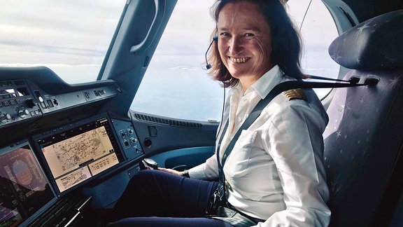Eine Frau sitzt im Cockpit eines Kleinflugzeuges und lächelt in die Kamera.