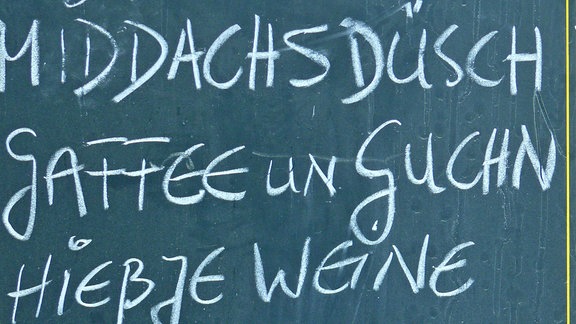 Eine grüne Tafel, auf der mit Kreide die sächsischen Wörter für Speisen und Getränke geschrieben stehen