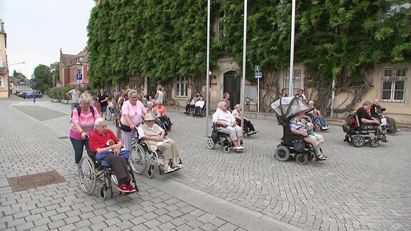 Eine Gruppe Menschen im Rollstuhl fahren durch eine Innenstadt.