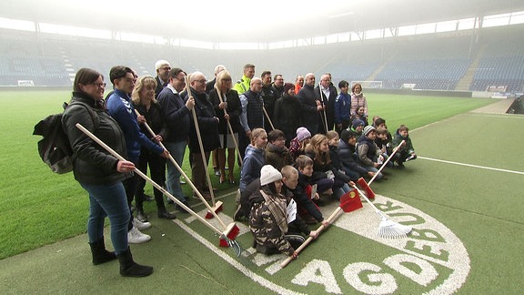 Menschen mit Besen im Stadion in Magdeburg