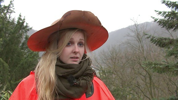 Eine junge Frau mit uasgefallenem Hut spricht in die Kamera.