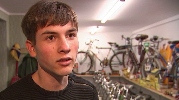 Ein junger Mann steht in einem Raum voller sortierter Fahrräder
