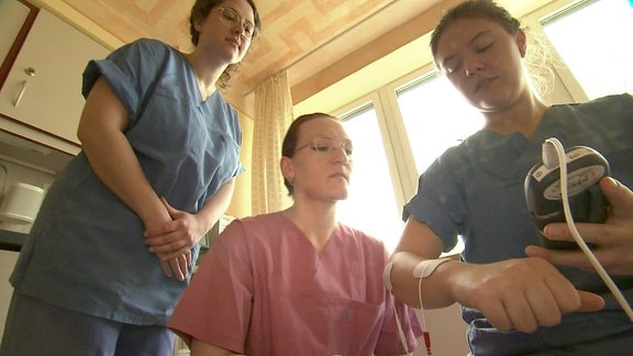 Drei Frauen in Dienstkleidung schauen auf ein Gerät.