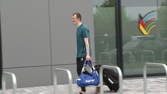 Ein Mann läuft mit Sporttaschen einen Weg entlang.