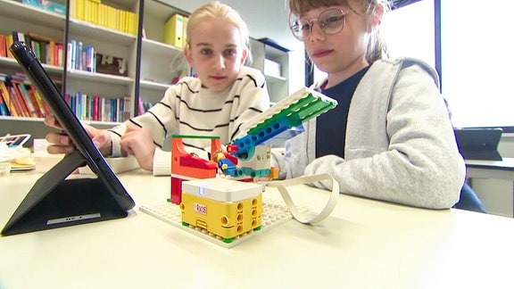 Zwei Mädchen beobachten einen Roboter, der aus Legosteinen gebaut wurde