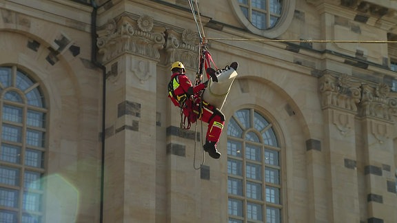 Ein Mitarbeiter des Rettungsdienst und eine Liege hängen an Seilen in der Luft.