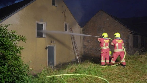 Zwei Feuerwehreinsatzkräfte spritzen Wasser in ein Fenster einer brennenden Pension 