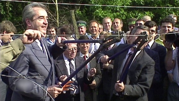 Ein östereichischer und ungarischer Minister durchtrennen einen Grenzzaun mit Bolzenschneidern.