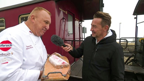 Ein Reporter interviewt einen Konditor mit Stollen auf dem Brocken