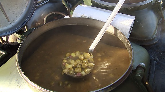 Eine Kelle voll mit Gulasch wird aus einem Topf geschöpft.