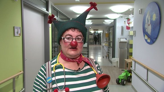 Eine Frau im Clownskostüm steht im Flur der Kinderstation.