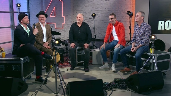 Mitglieder der Band Rockhaus und Moderator Peter Imhof sitzen im Studio und lachen herzlich.
