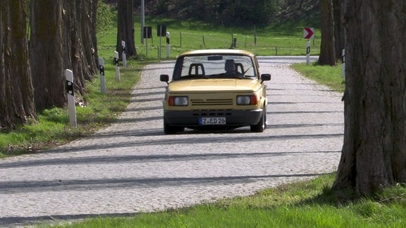 Ein gelber, tiefergelegter Wartburg fährt auf einer Straße.