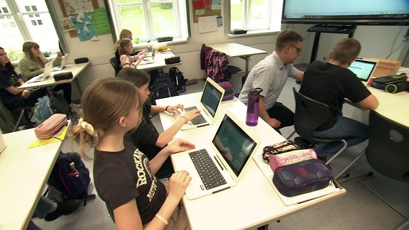 Schüler mit Laptops auf den Schultischen.