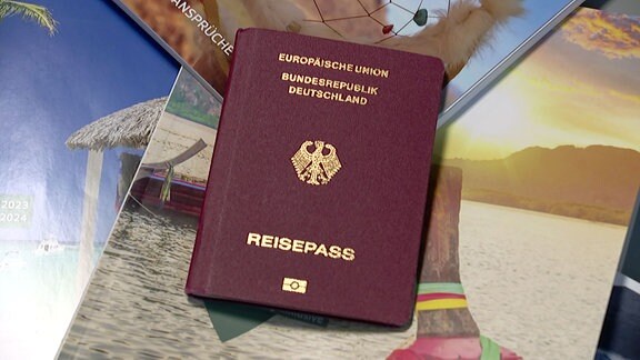 Ein Reisepass liegt auf Urlaubskatalogen.