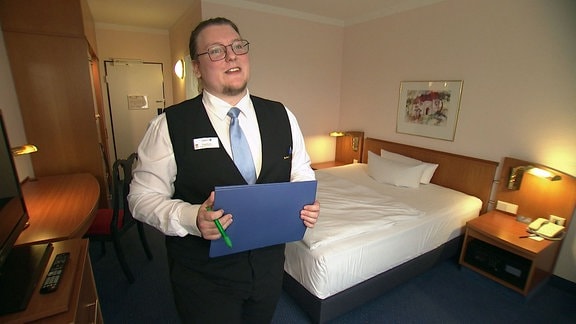 Hotelfachmann steht in einem Hotelzimmer.