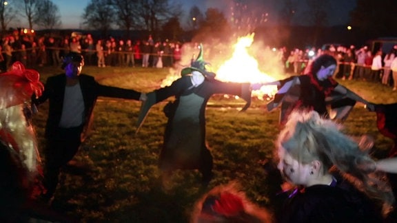 Frauen in Verkleidung tanzen um ein Feuer. 