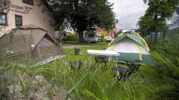 Zelte und Wohnwagen stehen auf dem Gelände neben einem Gebäude.