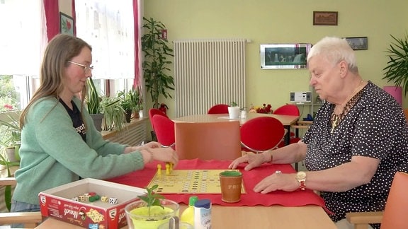 Junge Frau spielt mit älterer Frau ein Brettspiel.