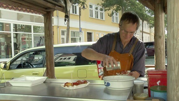 Ein Mann streut Currypulver auf eine Wurst.