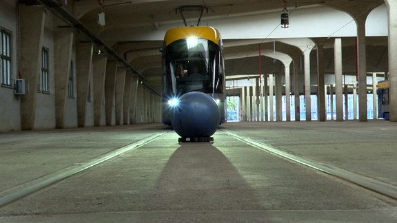 Eine Straßenbahn fährt auf einen blauen Gummiball zu.