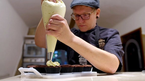 Erik Sachsenweger hantiert mit dem Spritzbeutel, bei der Zubereitung seiner Cupcakes.