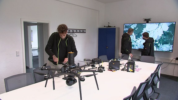 Menschen arbeiten an einer Drohne und schauen auf eine Karte