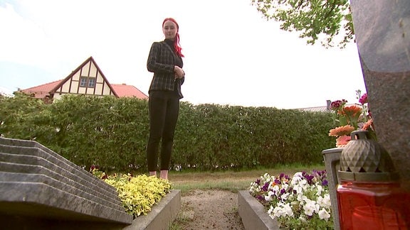 Eine junge Frau schaut auf ein Grab.