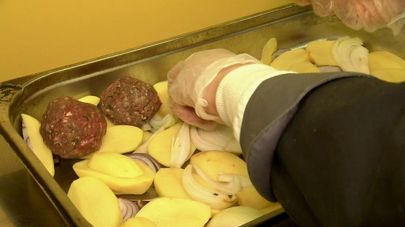 Eine Hand im Gummihandschuh legt Fleischbällchen auf Kartoffeln.