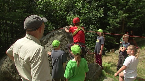 Gruppe Kinder und ein Ranger stehen um einen großen Stein. Ein Kind klettert auf den Stein.