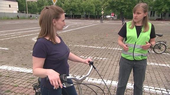 Eine Ausbilderin erklärt einer Frau das Radfahren auf einem Übungsplatz