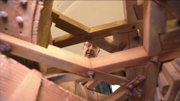 Ein Mann hinter einer Holzkonstruktion einer Mühle.