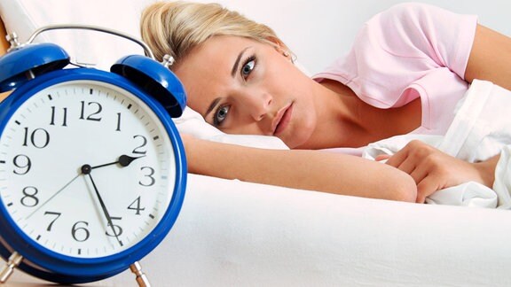 junge Frau liegt im Bett und schaut auf einen Wecker