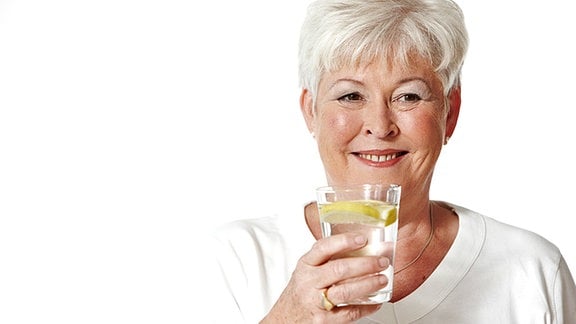 Eine grauhaarige Frau hat ein Glas Wasser mit Zitrone in der Hand