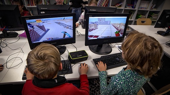 Zwei Kinder sitzen nebeneinander vor Computern und spielen Videospiele.