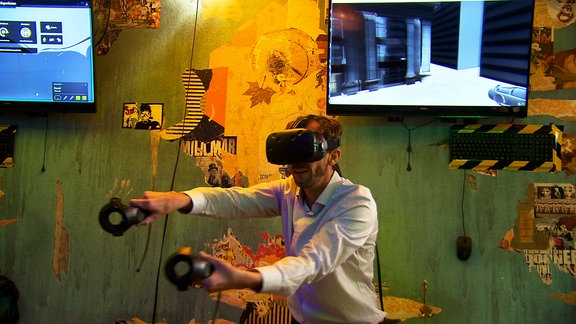 Gaming-Spaß in der virtuellen Welt: Ein Mann trägt eine VR-Brille und steuert mit zwei Controllern in den Händen ein Spiel bei dem man durch eine Stadt fliegt. 