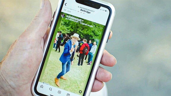 Ein Handy liegt in der Hand einer älteren Person. Auf dem Bildschirm ist ein Instagram-Video des "Granfluencers" Günther Anton Krabbenhöft zu sehen.