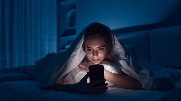 Frau surft nachts mit Smartphone im Bett.