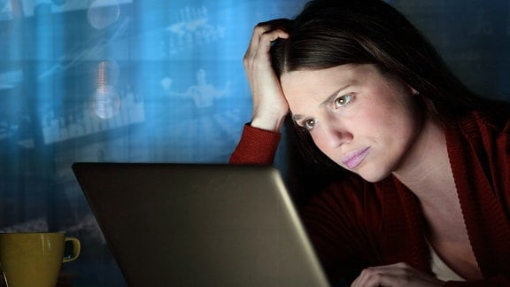 Eine Frau sitzt mit sorgenvollem Blick vor einem Laptop. Im Hintergrund ziehen Bilder von Nachrichten vorbei.