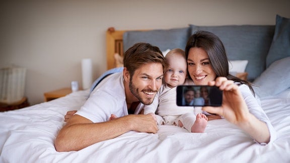 Ein Mann und eine Frau posieren mit ihrem Säugling für ein Selfie.