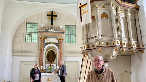 Drei Menschen stehen in der Zöschener Kirche. 