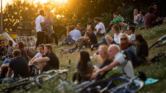 Dresden: Zahlreiche Menschen sitzen kurz vor Sonnenuntergang am Königsufer und hören die Musik vom Konzert nebenan