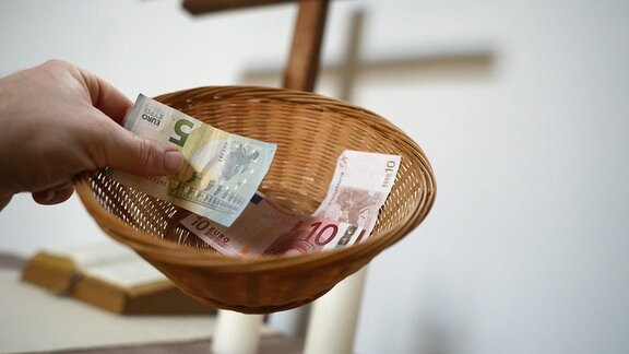 Eine Hand hält einen Sammelkorb mit Geld für die gottesdienstliche Kollekte. 