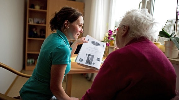 Die Ergotherapeutin Cornelia Rachold liest zusammen mit einer an Demenz erkrankten Frau die Seniorenheimzeitung im Zimmer der Bewohnerin im Seniorenheim Elbflorenz in Dresden