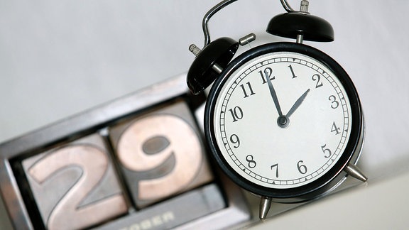 Zeitumstellung: ein Wecker zeigt zwei Uhr, im Hintergrund zeigt ein Kalender das Datum 29. Oktober.